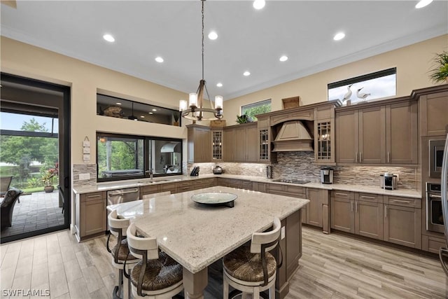 kitchen featuring a breakfast bar area, appliances with stainless steel finishes, light stone counters, custom range hood, and a kitchen island