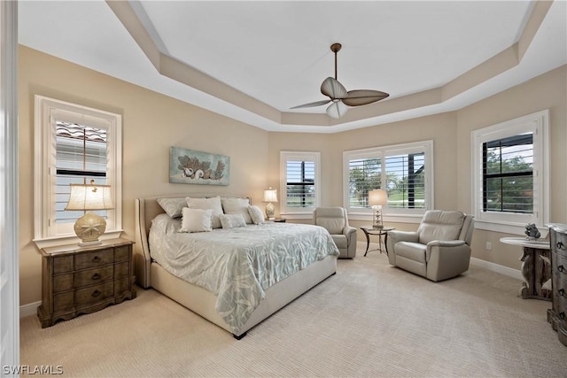 carpeted bedroom with ceiling fan, a tray ceiling, and multiple windows