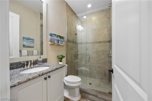 bathroom featuring vanity, hardwood / wood-style flooring, a shower with door, and toilet