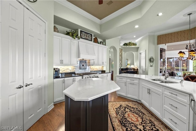 kitchen with arched walkways, premium range hood, a kitchen island, and ornamental molding