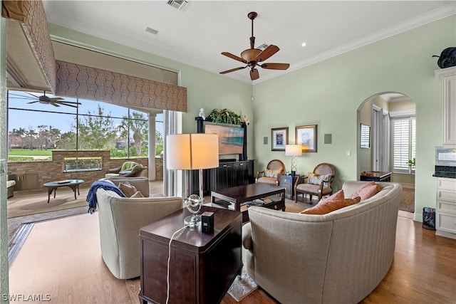 living area featuring arched walkways, ornamental molding, wood finished floors, and a ceiling fan