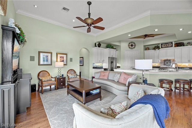 living room featuring arched walkways, crown molding, visible vents, and light wood-style floors