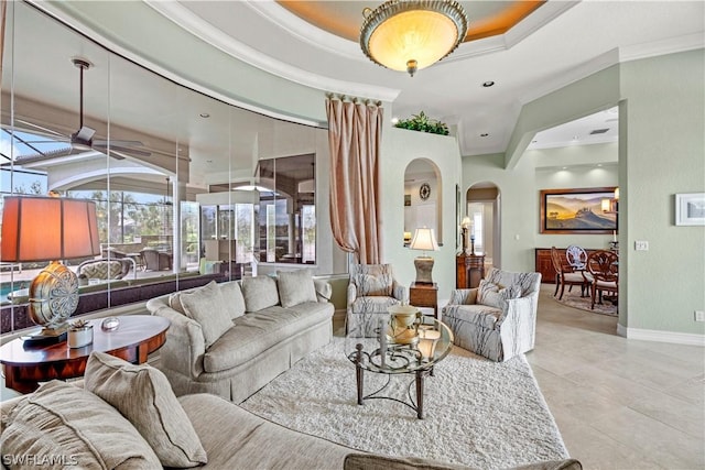 living room with light tile patterned floors, arched walkways, baseboards, a raised ceiling, and crown molding