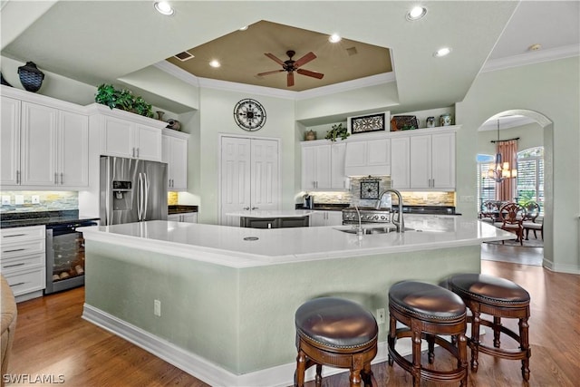 kitchen featuring arched walkways, wine cooler, a large island, a sink, and stainless steel fridge with ice dispenser