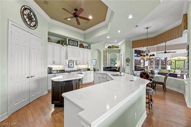 kitchen featuring arched walkways, ornamental molding, stainless steel gas range, a large island with sink, and a sink