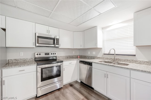 kitchen with a paneled ceiling, stainless steel appliances, hardwood / wood-style floors, white cabinets, and sink