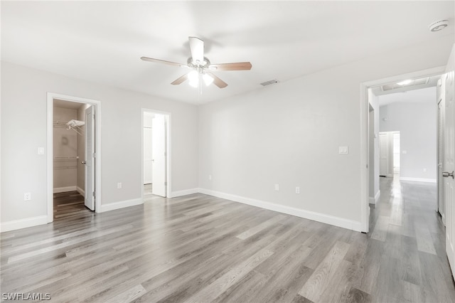 unfurnished bedroom featuring a spacious closet, ceiling fan, light hardwood / wood-style flooring, and a closet