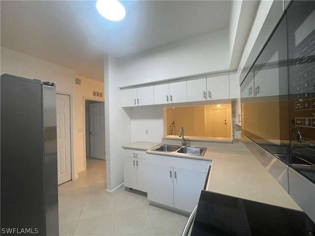 kitchen with stainless steel refrigerator, sink, white cabinets, and light tile patterned floors