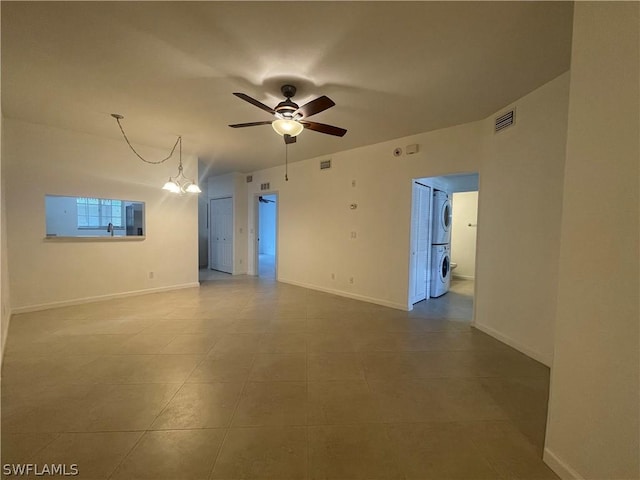 spare room featuring ceiling fan with notable chandelier and stacked washer and clothes dryer