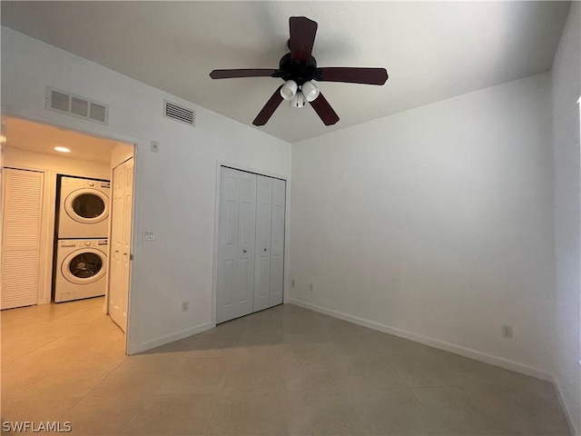 unfurnished bedroom with stacked washer / dryer, ceiling fan, a closet, and light tile patterned floors