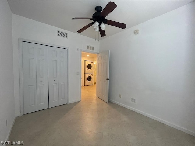 unfurnished bedroom with a closet, ceiling fan, stacked washer and clothes dryer, and light tile patterned flooring