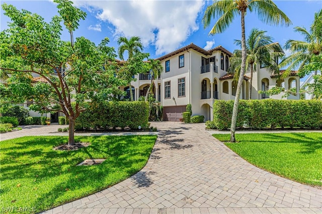 mediterranean / spanish-style home with a garage, a balcony, and a front lawn