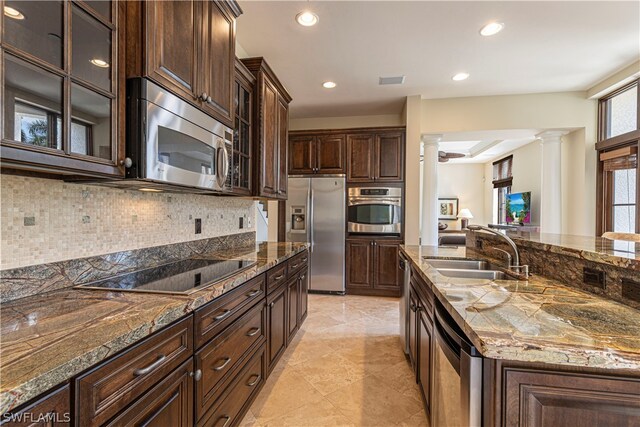 kitchen with appliances with stainless steel finishes, ornate columns, dark stone counters, sink, and dark brown cabinets