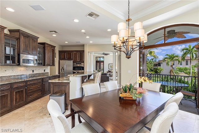 dining space with crown molding, ceiling fan with notable chandelier, and ornate columns