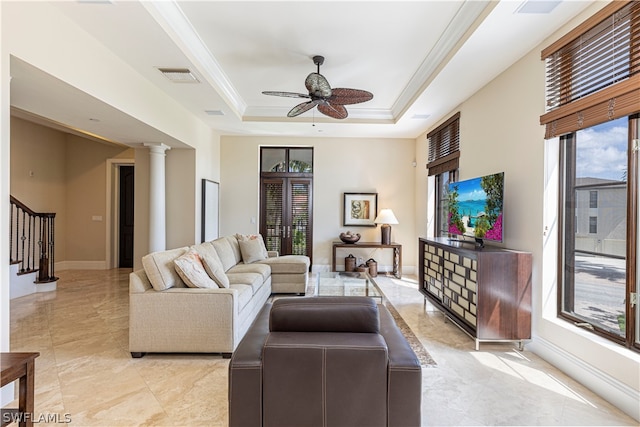 living room featuring ceiling fan, crown molding, a tray ceiling, and ornate columns