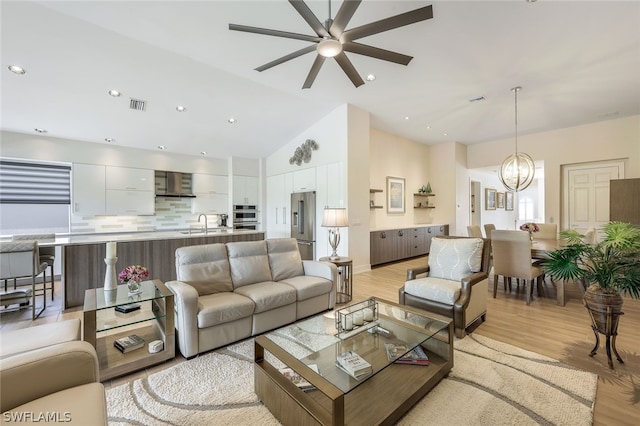 living room featuring ceiling fan with notable chandelier, vaulted ceiling, and light hardwood / wood-style floors