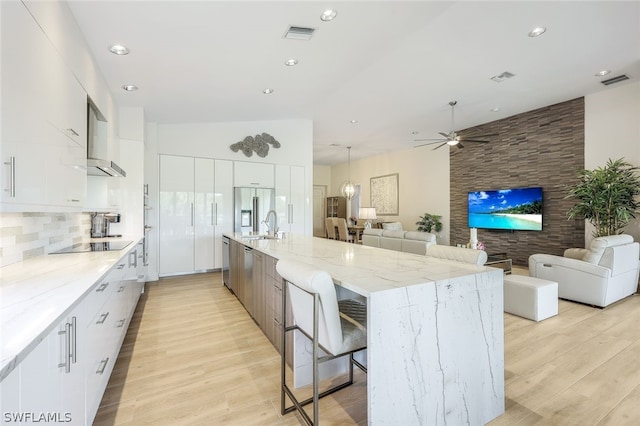 kitchen featuring light stone counters, a spacious island, light hardwood / wood-style floors, white cabinets, and appliances with stainless steel finishes