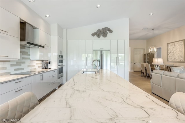 kitchen with sink, white cabinetry, wall chimney exhaust hood, hanging light fixtures, and appliances with stainless steel finishes