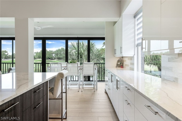 kitchen with white cabinets, light hardwood / wood-style floors, tasteful backsplash, light stone countertops, and dark brown cabinetry