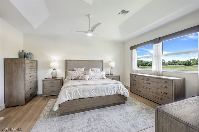 bedroom with ceiling fan, a tray ceiling, and light hardwood / wood-style flooring