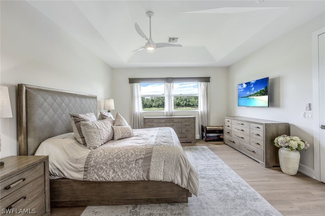 bedroom with light hardwood / wood-style floors, ceiling fan, and a tray ceiling