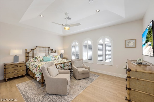 bedroom featuring ceiling fan, light wood-type flooring, and a tray ceiling