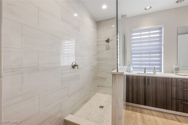 bathroom with hardwood / wood-style floors, tiled shower, and vanity