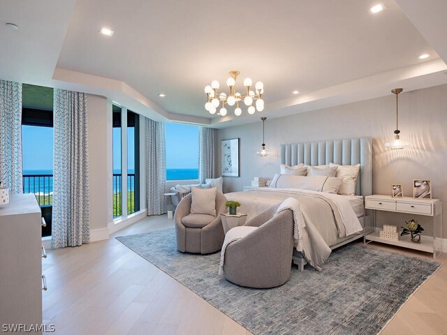 bedroom featuring a water view, access to outside, hardwood / wood-style flooring, a raised ceiling, and a notable chandelier