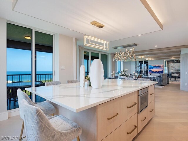 kitchen with light stone counters, decorative light fixtures, a kitchen breakfast bar, a large island, and light brown cabinetry