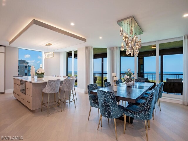 dining space featuring an inviting chandelier, a water view, light wood-type flooring, and a wall of windows