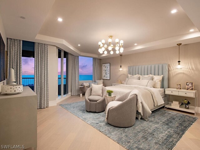 bedroom with an inviting chandelier, a water view, wood-type flooring, and a raised ceiling