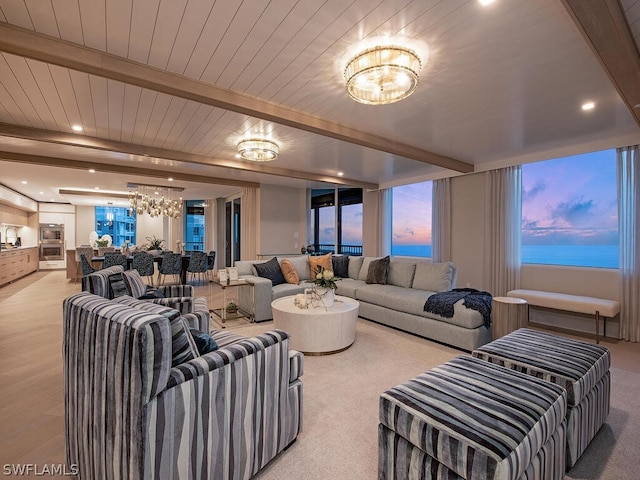 living room featuring beamed ceiling, a water view, light wood-type flooring, and a notable chandelier