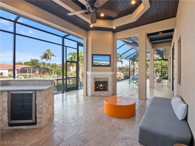 sunroom featuring a tray ceiling, a warm lit fireplace, wooden ceiling, and ceiling fan