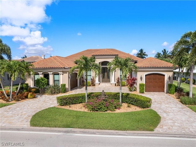 mediterranean / spanish house featuring a garage, stucco siding, decorative driveway, and a tiled roof