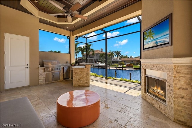 sunroom / solarium featuring a ceiling fan, a glass covered fireplace, wood ceiling, and a water view