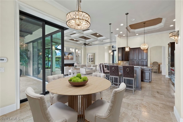 dining space with arched walkways, crown molding, coffered ceiling, a lit fireplace, and ceiling fan with notable chandelier