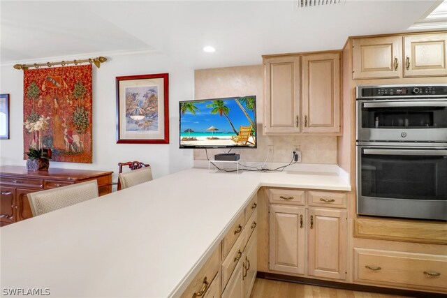 kitchen featuring stainless steel double oven, light brown cabinets, kitchen peninsula, light hardwood / wood-style flooring, and crown molding