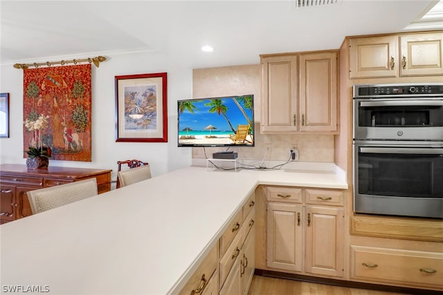 kitchen featuring light countertops, backsplash, light brown cabinetry, stainless steel double oven, and light wood-type flooring