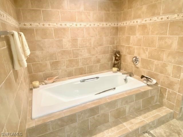 bathroom with a relaxing tiled tub and tile walls