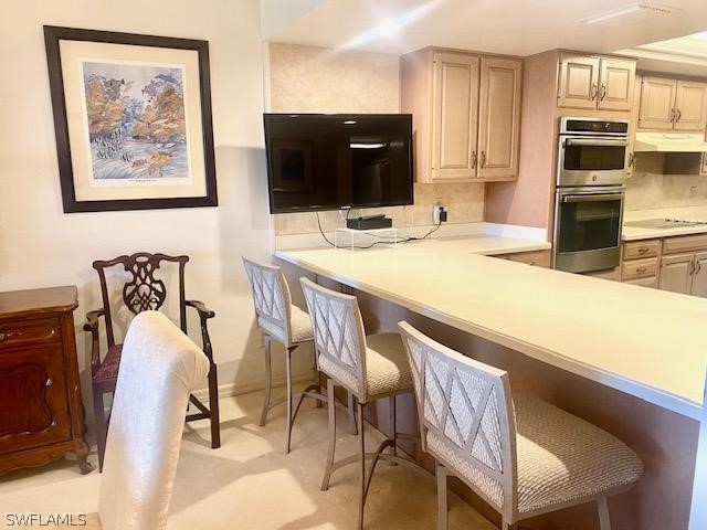 kitchen featuring light brown cabinets, double oven, kitchen peninsula, a breakfast bar, and black electric cooktop