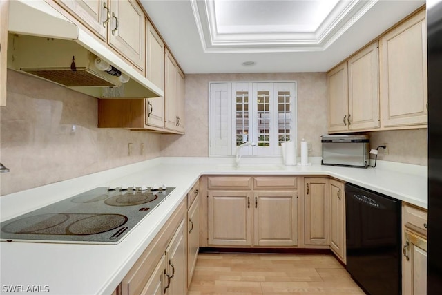 kitchen with under cabinet range hood, light brown cabinetry, light wood-type flooring, black appliances, and a tray ceiling