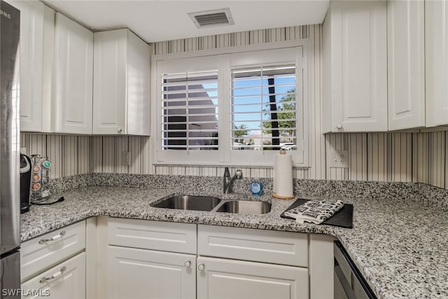 kitchen with sink, stainless steel fridge, white cabinetry, and light stone countertops