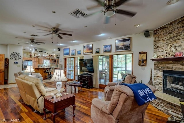 living room featuring hardwood / wood-style floors, a stone fireplace, and ceiling fan