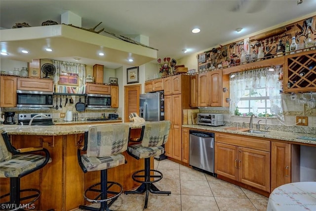 kitchen featuring light stone counters, appliances with stainless steel finishes, a kitchen breakfast bar, and sink