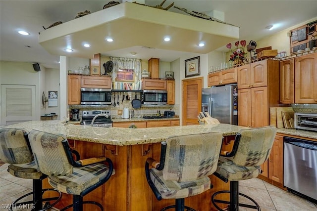 kitchen featuring light tile patterned flooring, a kitchen breakfast bar, a large island with sink, and appliances with stainless steel finishes