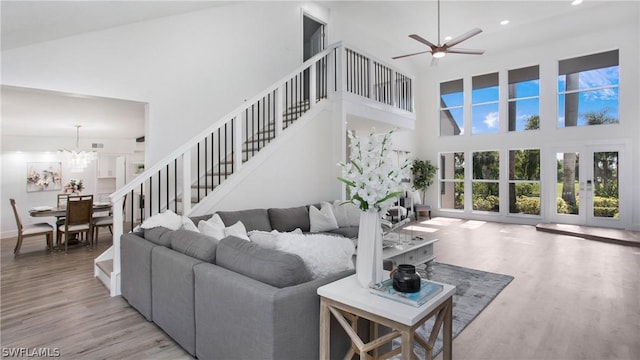 living room with french doors, ceiling fan with notable chandelier, a high ceiling, and light wood-type flooring