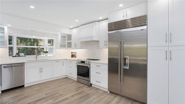 kitchen with sink, white cabinetry, stainless steel appliances, and custom range hood