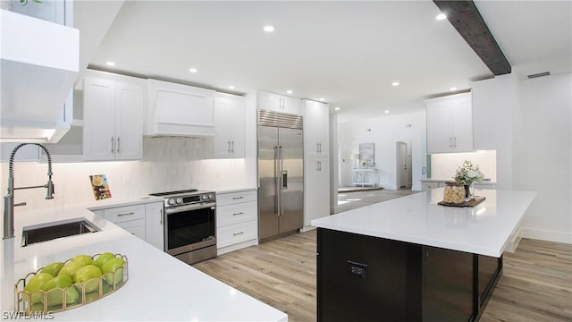 kitchen featuring light wood-type flooring, custom range hood, stainless steel appliances, sink, and white cabinetry