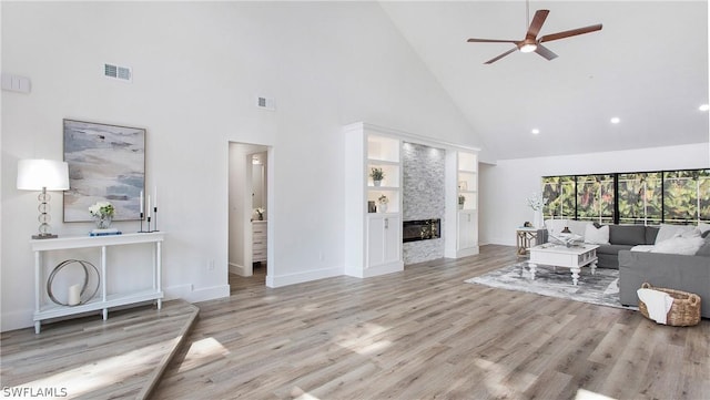 living room featuring ceiling fan, high vaulted ceiling, built in features, light hardwood / wood-style flooring, and a fireplace