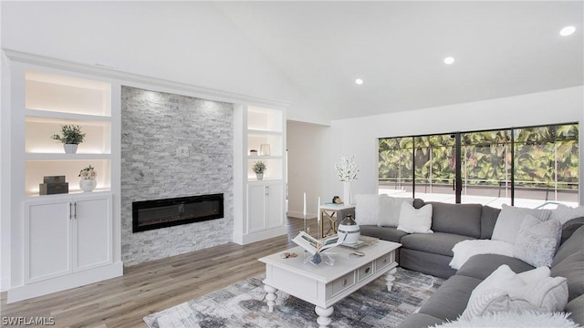 living room with hardwood / wood-style floors, a stone fireplace, built in features, and high vaulted ceiling